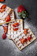 Image showing Belgium waffers with strawberries and sugar powder on black boar