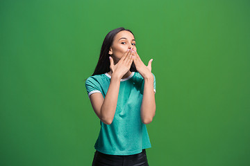 Image showing The young woman whispering a secret behind her hand over green background