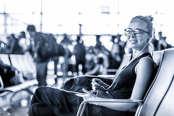 Image showing Female traveler using her cell phone while waiting to board a plane at departure gates at asian airport terminal. Blue toned black and white photo.