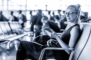 Image showing Female traveler using her cell phone while waiting to board a plane at departure gates at asian airport terminal. Blue toned black and white photo.