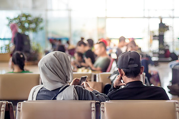 Image showing Modern muslim islamic asian couple using their smartphone apps while sitting and waiting for flight departure at international airport terminal