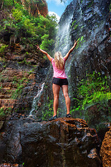 Image showing Woman stands on rock in front of cascading waterfall