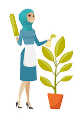 Image showing Young muslim housemaid watering flower with spray.