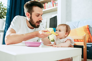 Image showing Good looking young man eating breakfast and feeding her baby girl at home