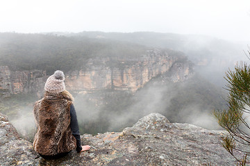 Image showing Female sitting on mountain top cliff ledge looking out into the misty fog