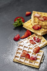 Image showing Belgium waffers with strawberries and sugar powder on black boar