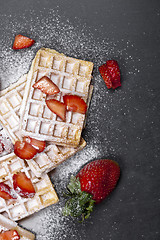 Image showing Belgium waffers with strawberries and sugar powder on black boar