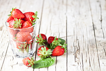 Image showing Organic red strawberries in glass and mint leaves on rustic wood