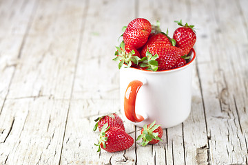 Image showing Organic red strawberries in white ceramic cup on rustic wooden b