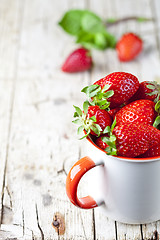 Image showing Organic red strawberries in white ceramic cup on rustic wooden b