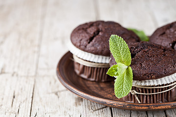 Image showing Chocolate dark muffins with mint leaves on brown ceramic plate.