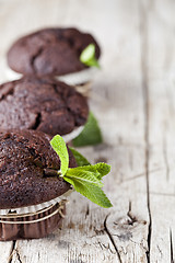 Image showing Chocolate dark muffins with mint leaves closeup on rustic wooden