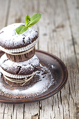 Image showing Chocolate dark muffins with sugar powder and mint leaf on brown 