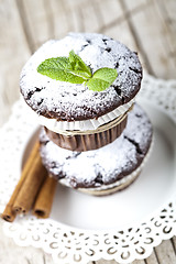 Image showing Chocolate dark muffins with sugar powder, cinnamon sticks and mi