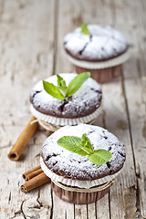 Image showing Chocolate dark muffins with sugar powder, cinnamon sticks and mi