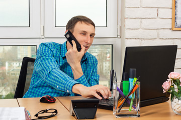 Image showing Young office worker talking on the phone and working in a laptop