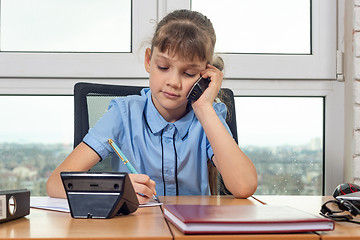 Image showing Eight-year-old girl talking on the phone at the table in the office