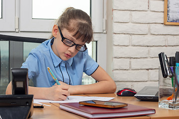 Image showing An eight-year-old girl at the table in the office writes a fountain pen on a piece of paper