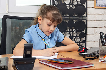 Image showing An eight-year girl writes on a sheet of paper at a table in the office