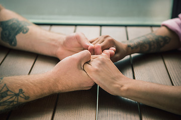 Image showing Close up on a man and a woman holding hands at a wooden table
