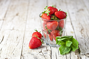 Image showing Organic red strawberries glass and mint leaves on rustic wooden 