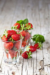 Image showing Organic red strawberries in two glasses and mint leaves on rusti