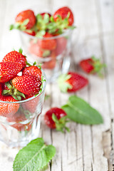 Image showing Organic red strawberries in two glasses and mint leaves on rusti