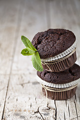 Image showing Chocolate dark muffins with mint leaves on rustic wooden table.