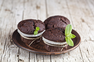 Image showing Three chocolate dark muffins with mint leaves on brown ceramic p