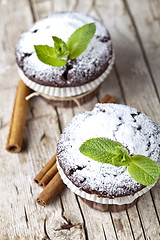 Image showing Dark chocolate muffins with sugar powder, cinnamon sticks and mi