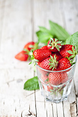 Image showing Organic red strawberries in glass and mint leaves on rustic wood