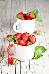 Image showing Organic red strawberries in two white ceramic cups and mint leav