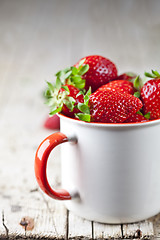 Image showing Organic red strawberries in white ceramic cup on rustic wooden b