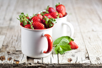 Image showing Organic red strawberries in two white ceramic cups and mint leav