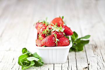 Image showing Fresh red strawberries in white bowl and mint leaves on rustic w