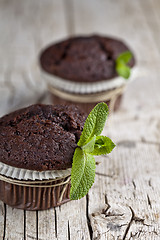 Image showing Chocolate dark muffins with mint leaves closeup on rustic wooden
