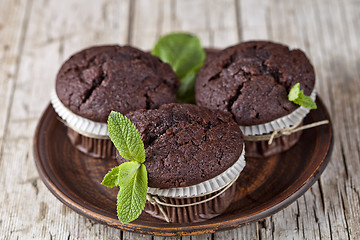 Image showing Three chocolate dark muffins with mint leaves on brown ceramic p