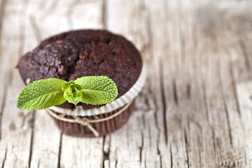 Image showing Chocolate dark muffins with mint leaves on rustic wooden table.