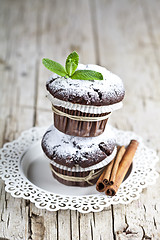 Image showing Chocolate dark muffins with sugar powder, cinnamon sticks and mi