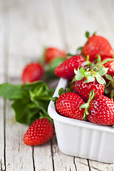 Image showing Fresh red strawberries in white bowl and mint leaves on rustic w