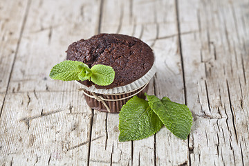 Image showing Fresh dark chocolate muffin with mint leaves on rustic wooden ta