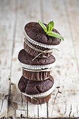 Image showing Three fresh dark chocolate muffins with mint leaves on rustic wo