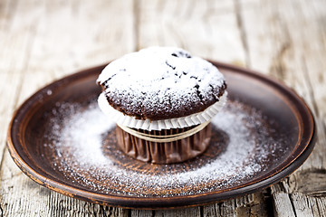 Image showing Dark chocolate muffin with sugar powder on brown plate.