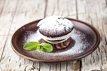 Image showing Fresh chocolate dark muffin with sugar powder and mint leaf on b