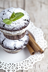 Image showing Chocolate dark muffins with sugar powder, cinnamon sticks and mi