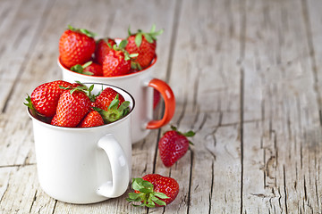 Image showing Organic red strawberries in two white ceramic cups on rustic woo