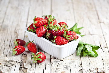 Image showing Fresh red strawberries in white bowl and mint leaves on rustic w