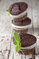 Image showing Three fresh dark chocolate muffins with mint leaves on rustic wo