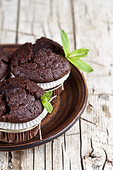 Image showing Chocolate dark muffins with mint leaves on brown ceramic plate c