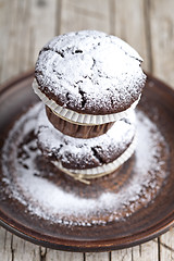 Image showing Dark chocolate muffins with sugar powder on brown plate on rusti